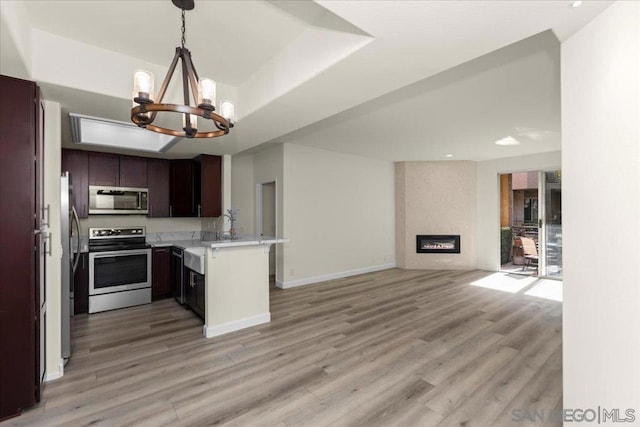 kitchen featuring dark brown cabinetry, light hardwood / wood-style flooring, a large fireplace, appliances with stainless steel finishes, and kitchen peninsula