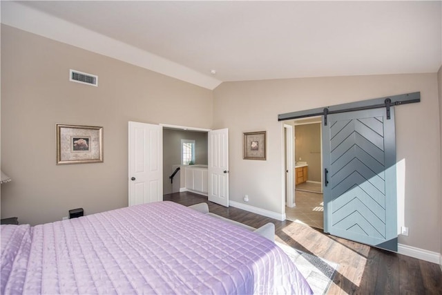 bedroom with connected bathroom, a barn door, dark wood-type flooring, and lofted ceiling