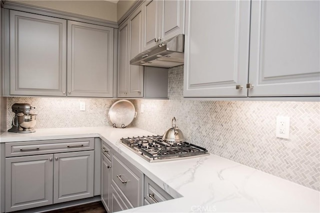 kitchen featuring stainless steel gas stovetop, backsplash, light stone countertops, and gray cabinets