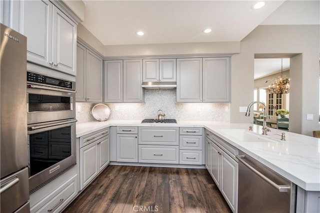 kitchen featuring appliances with stainless steel finishes, sink, kitchen peninsula, dark hardwood / wood-style flooring, and light stone counters