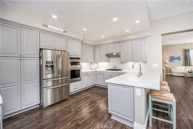 kitchen featuring kitchen peninsula, a kitchen breakfast bar, appliances with stainless steel finishes, sink, and gray cabinets