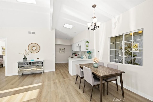 dining space featuring a towering ceiling, sink, a chandelier, and light wood-type flooring