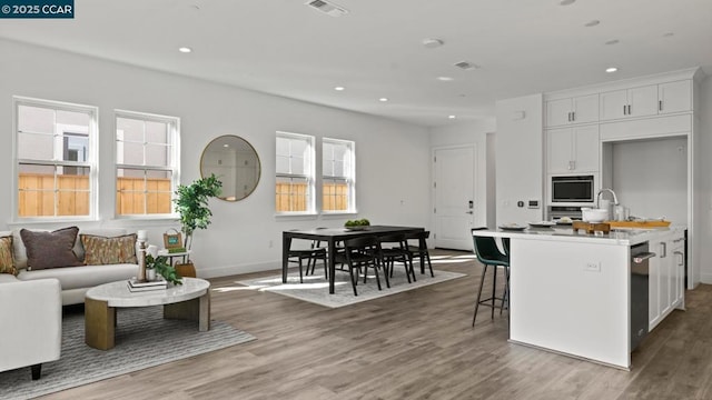 kitchen featuring a kitchen breakfast bar, a center island with sink, white cabinets, and hardwood / wood-style flooring