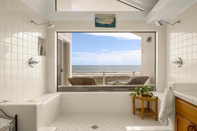 bathroom with vanity, a water view, a view of the beach, and walk in shower