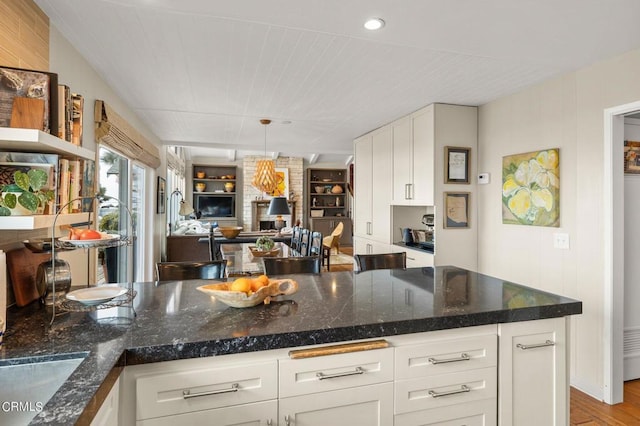 kitchen featuring dark stone countertops, white cabinetry, hanging light fixtures, and light hardwood / wood-style flooring