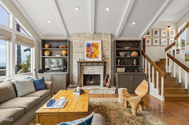 living room with wood-type flooring, lofted ceiling with beams, and a fireplace