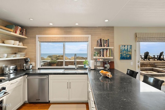 kitchen featuring decorative backsplash, sink, white cabinets, and a water view