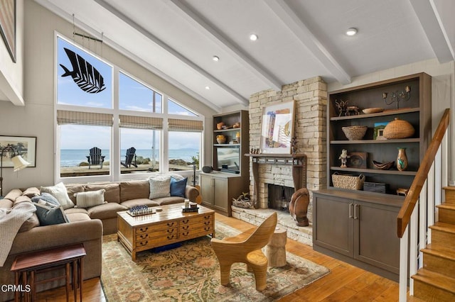 living room featuring built in features, light wood-type flooring, a water view, a fireplace, and vaulted ceiling with beams