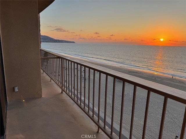 balcony at dusk with a water view and a view of the beach