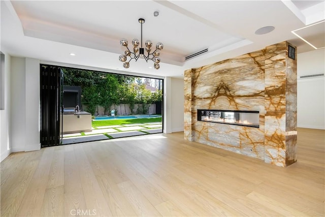 unfurnished living room featuring wood-type flooring, a tray ceiling, a notable chandelier, and a fireplace