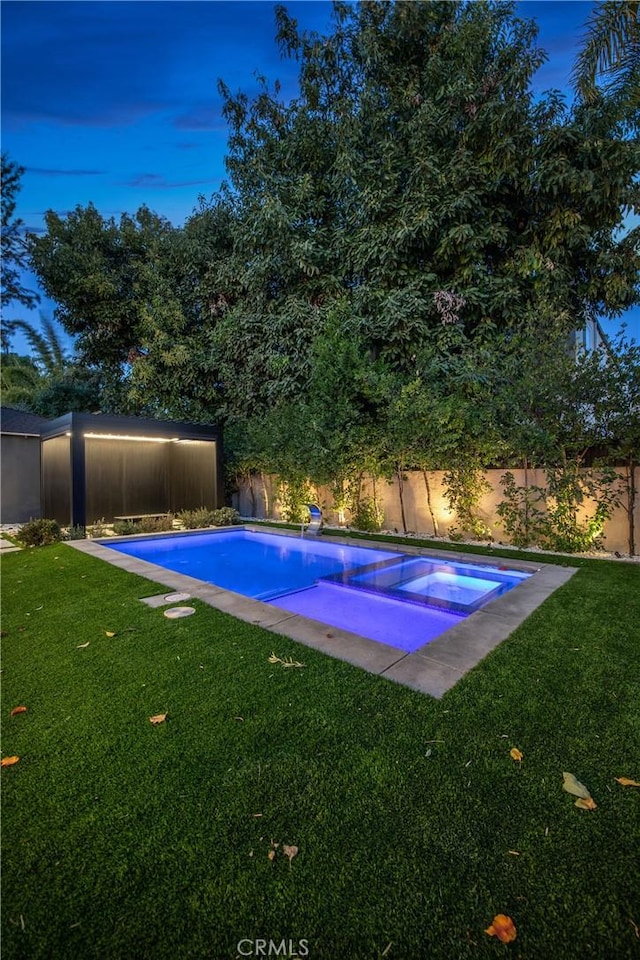 pool at dusk featuring an in ground hot tub and a yard