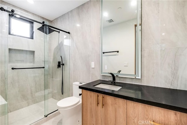 bathroom featuring vanity, toilet, tile walls, and a shower with door