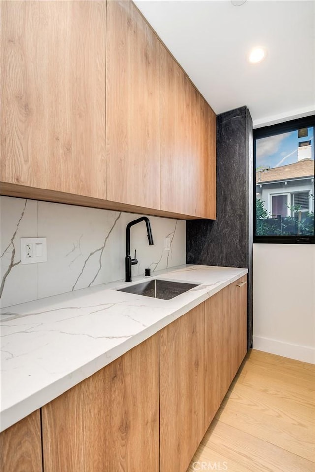 kitchen featuring light stone counters, sink, backsplash, and light wood-type flooring