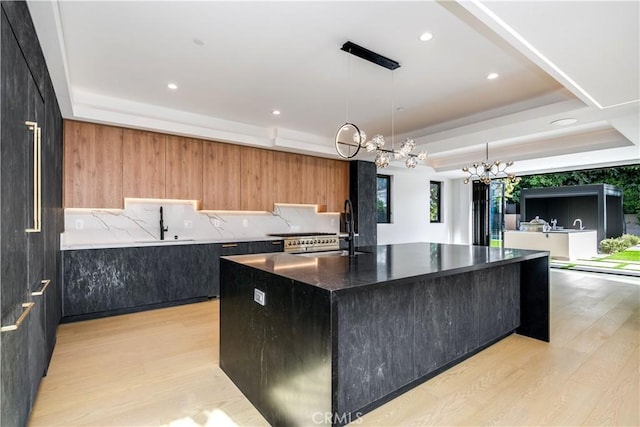 kitchen featuring light hardwood / wood-style floors, sink, pendant lighting, a center island with sink, and a tray ceiling