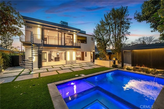 back house at dusk with a balcony, a swimming pool with hot tub, and a patio