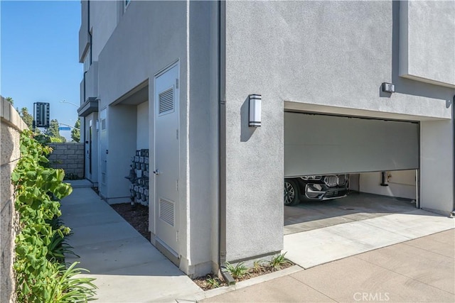 view of property exterior with stucco siding, an attached garage, concrete driveway, and fence