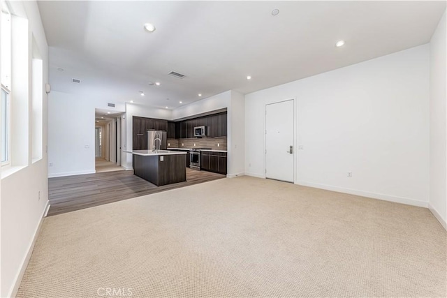 kitchen featuring an island with sink, recessed lighting, decorative backsplash, dark brown cabinetry, and open floor plan