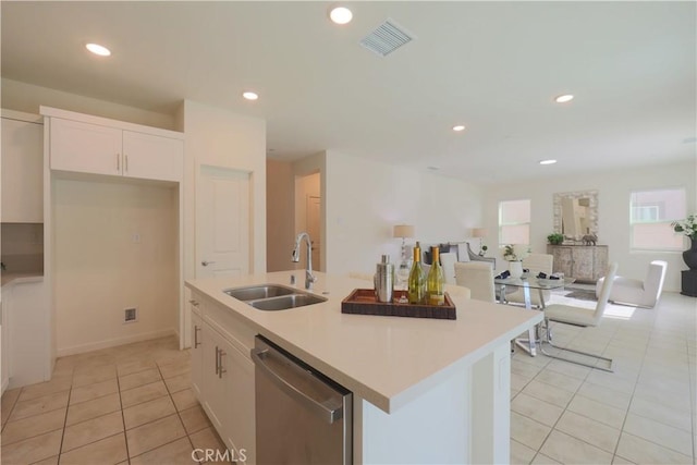 kitchen featuring dishwasher, sink, white cabinets, light tile patterned floors, and a center island with sink