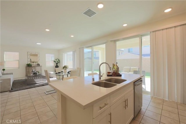 kitchen featuring a kitchen island with sink, light tile patterned floors, stainless steel dishwasher, sink, and white cabinets