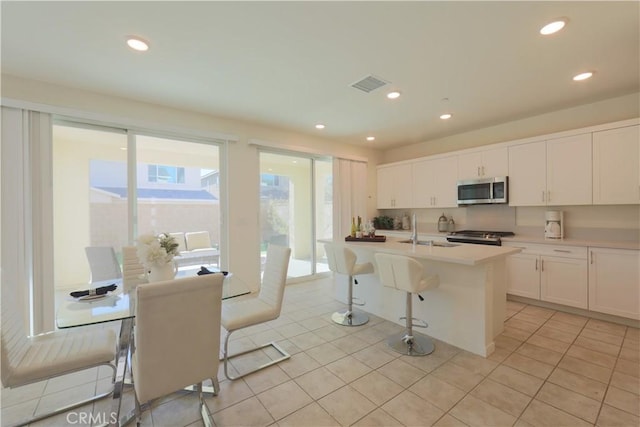 kitchen with white cabinetry, light tile patterned floors, a center island with sink, a breakfast bar area, and stainless steel appliances