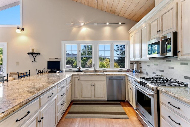 kitchen with sink, appliances with stainless steel finishes, tasteful backsplash, light stone countertops, and light hardwood / wood-style floors