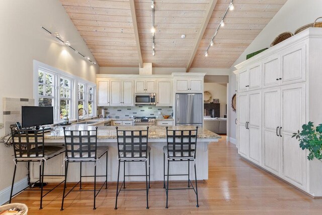 kitchen with wood ceiling, appliances with stainless steel finishes, a breakfast bar, and light stone countertops