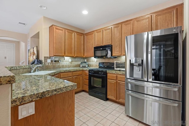 kitchen with black appliances, sink, kitchen peninsula, light tile patterned flooring, and stone counters