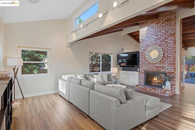 living room featuring light wood-type flooring, high vaulted ceiling, beam ceiling, and a fireplace