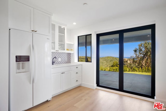 kitchen featuring white fridge with ice dispenser, white cabinets, backsplash, and light hardwood / wood-style flooring