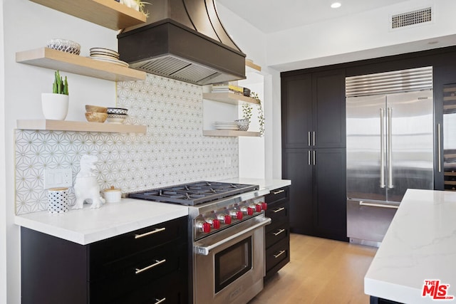 kitchen featuring light hardwood / wood-style flooring, high quality appliances, tasteful backsplash, island range hood, and light stone countertops