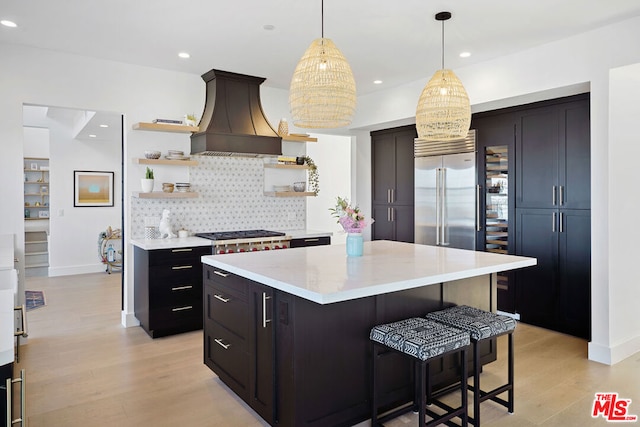 kitchen with a center island, custom range hood, stainless steel appliances, light hardwood / wood-style floors, and decorative backsplash