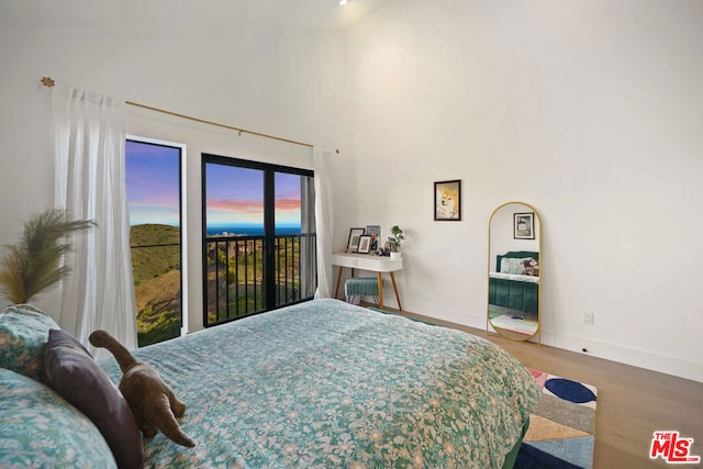 bedroom with a towering ceiling, hardwood / wood-style floors, and access to exterior