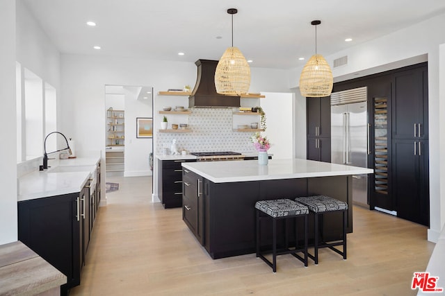 kitchen featuring appliances with stainless steel finishes, sink, custom exhaust hood, hanging light fixtures, and light wood-type flooring