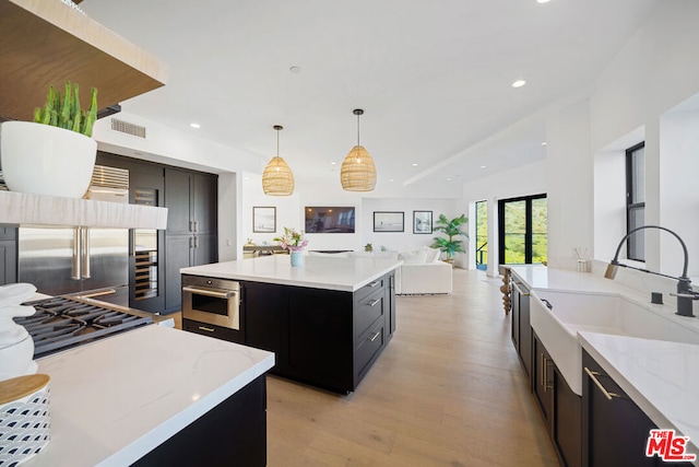 kitchen with sink, decorative light fixtures, a kitchen island, stainless steel appliances, and light hardwood / wood-style floors