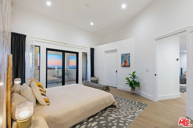 bedroom featuring french doors, access to exterior, light hardwood / wood-style floors, and a high ceiling