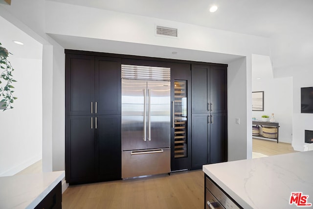 kitchen featuring light stone counters, stainless steel built in fridge, and light wood-type flooring