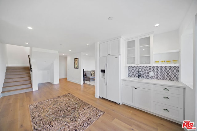 kitchen featuring sink, white refrigerator with ice dispenser, light hardwood / wood-style floors, and white cabinets