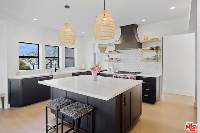 kitchen with custom range hood, sink, stainless steel gas cooktop, and light hardwood / wood-style floors