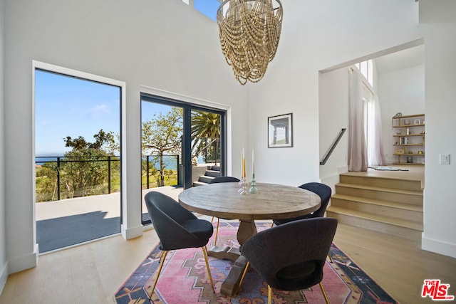 dining area with plenty of natural light, a towering ceiling, a chandelier, and light hardwood / wood-style floors