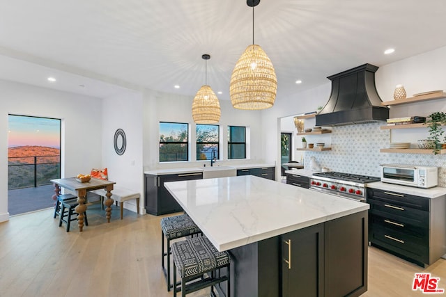 kitchen featuring a kitchen island, decorative light fixtures, backsplash, custom exhaust hood, and light hardwood / wood-style flooring