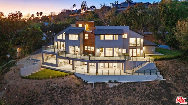 back house at dusk with a balcony and a patio