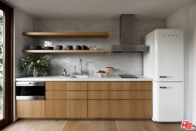 bar with wall chimney range hood, white refrigerator, decorative backsplash, sink, and stainless steel oven