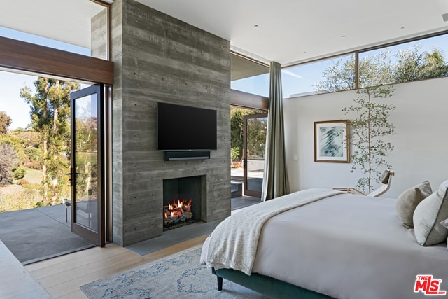 bedroom with light hardwood / wood-style floors, access to exterior, a wall of windows, and a fireplace