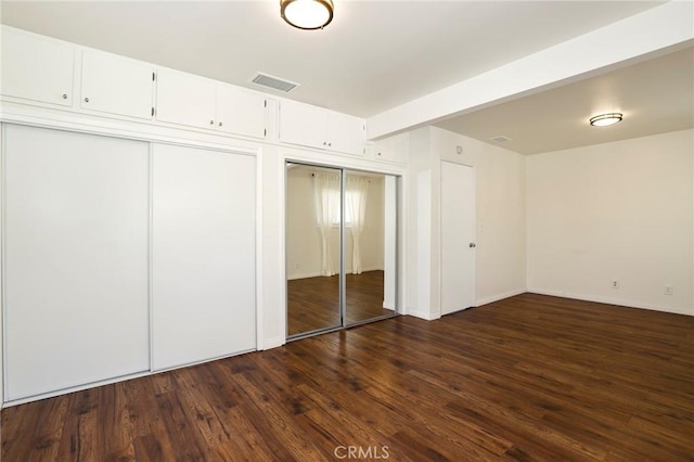 unfurnished bedroom with two closets, dark hardwood / wood-style flooring, and beamed ceiling