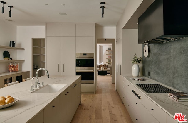 kitchen featuring double oven, tasteful backsplash, light hardwood / wood-style floors, sink, and light stone counters