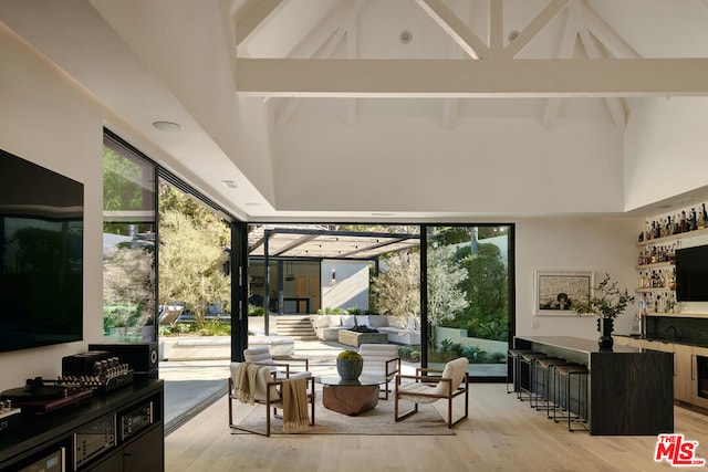 living room featuring bar, beamed ceiling, a healthy amount of sunlight, and light hardwood / wood-style floors