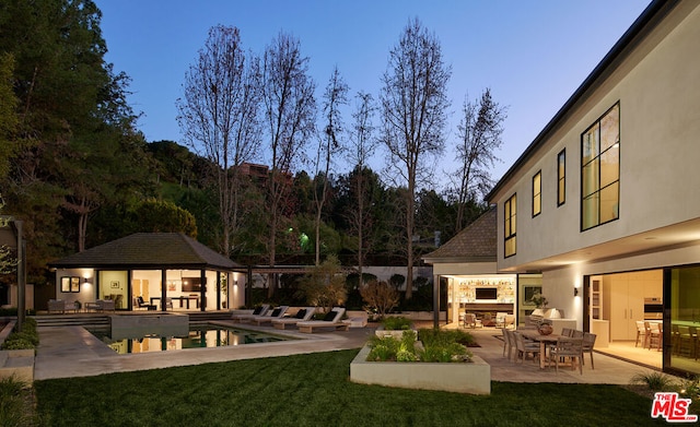 yard at dusk featuring an outdoor fireplace, a patio, and an outbuilding