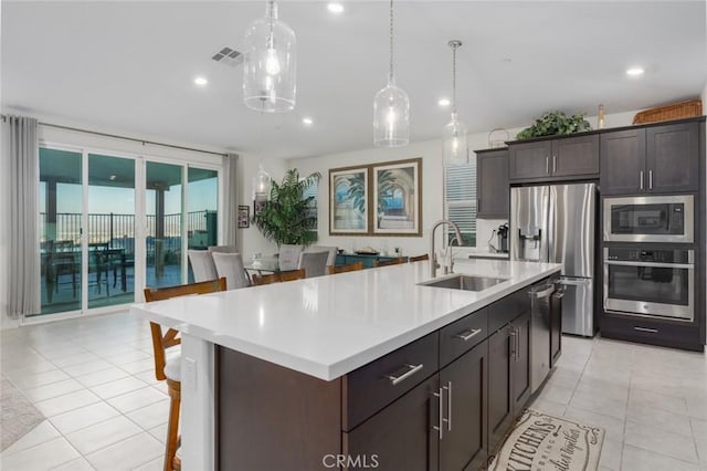 kitchen featuring sink, a center island with sink, stainless steel appliances, and dark brown cabinets