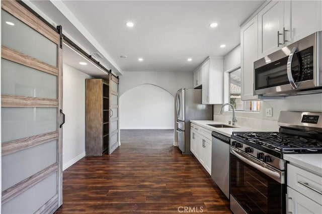 kitchen featuring white cabinetry, dark hardwood / wood-style flooring, stainless steel appliances, sink, and a barn door