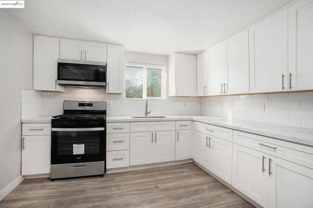 kitchen with appliances with stainless steel finishes, white cabinets, light wood-type flooring, sink, and light stone counters